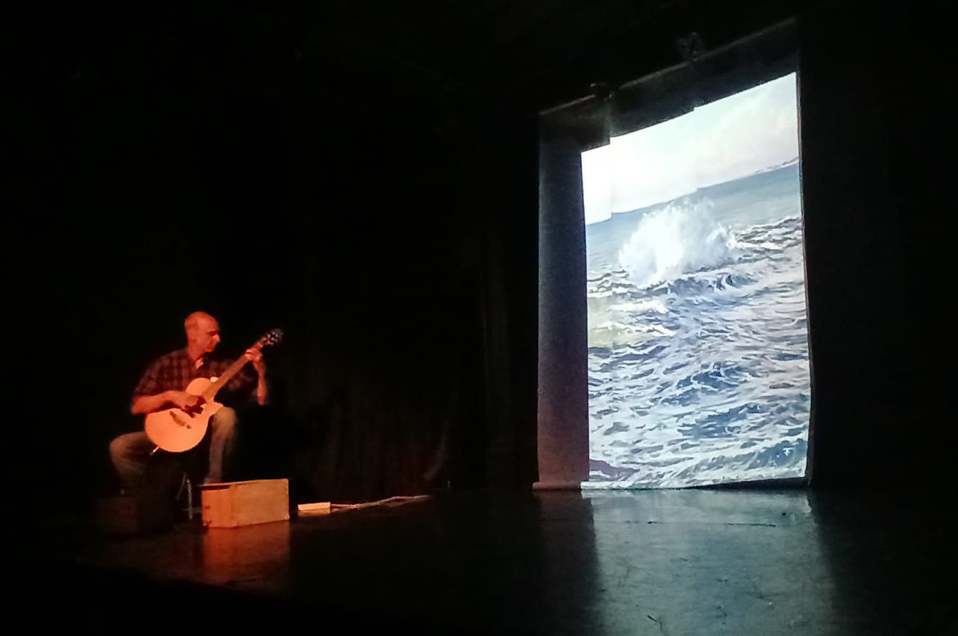 François Bihorel à la guitare sur scène, devant la projection d'une gouache de mer